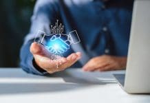 Has AI killed the approved supplier list? Close-up of a businessman with an open palm supporting a glowing digital hologram of a handshake between a human and an artificial intelligence robot, symbolizing tech partnership, digital transformation, and human-AI collaboration