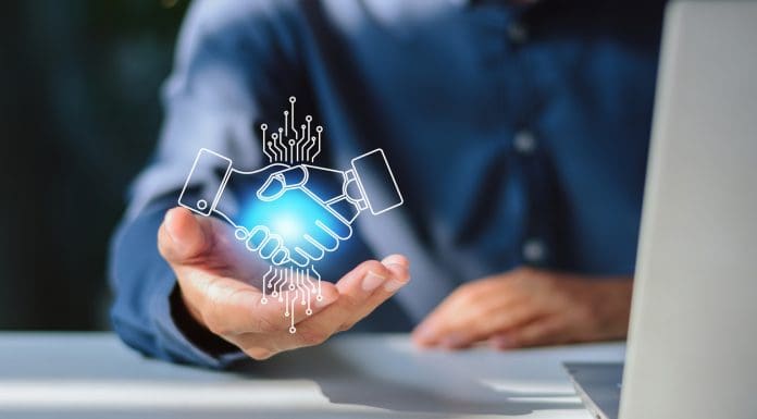 Close-up of a businessman with an open palm supporting a glowing digital hologram of a handshake between a human and an artificial intelligence robot, symbolizing tech partnership, digital transformation, and human-AI collaboration