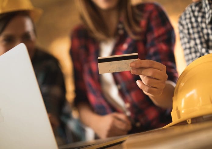 Close up of manual workers using credit card for online shopping. UK subcontractors still stung by constant late payments, report finds