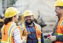 Drugs and alcohol on site: Policy and practicalities A group of three multi-ethnic workers at a construction site wearing hard hats, safety glasses and reflective clothing, smiling and conversing. The main focus is on the mixed race African-American and Pacific Islander man in the middle. The other two construction workers, including the woman, are Hispanic.