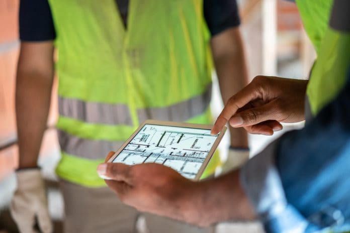 Construction site engineer reviewing blueprints on digital tablet Digital construction productivity: Measuring real value