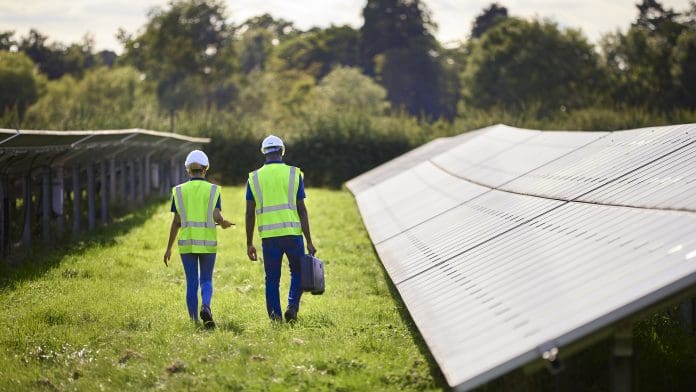 Rear View Of Male And Female Engineers Inspecting Solar Panels In Field Generating Renewable Energy Social licence will be crucial to meeting the UK’s clean energy goals