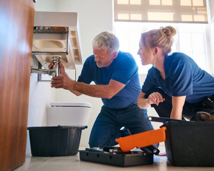 Male Plumber Fixing Leak In Domestic Bathroom Sink With Female Trainee Holding Digital Tablet Scotland faces apprenticeship crisis as plumbing and heating pull back hires