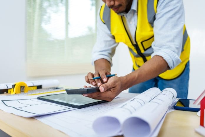 Asian male architect works at desk with house model toy and A3 paper blueprints, construction real estate law, zoning, permits, and resolving property disputes through arbitration and litigation. Payapps further explores Subcontractor payment applications