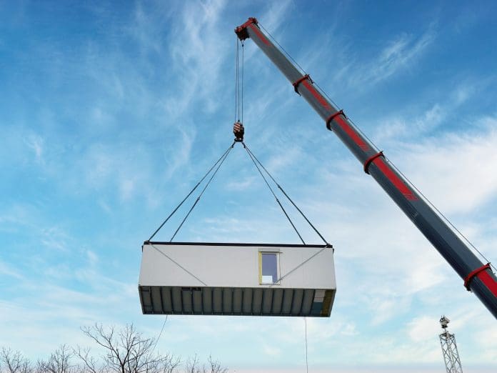 large crane lifting a prefabricated modular building unit against a bright blue sky Designing the nation’s schools for a low-carbon future with reuse in mind