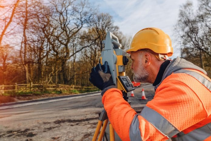 Construction worker uses surveying equipment in a wooded area to measure and plan roadwork during the day The future of the surveying industry is about more than capturing data